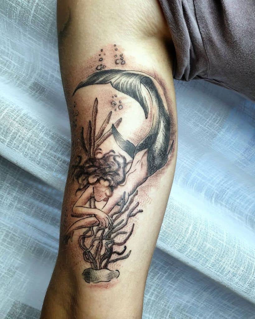 Intricate arm tattoo of a mermaid swimming among seaweed and bubbles, featuring a detailed tail and flowing hair