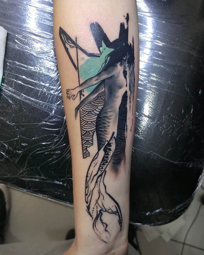Abstract forearm tattoo of a mermaid with bold black and green accents, blending geometric and flowing design elements