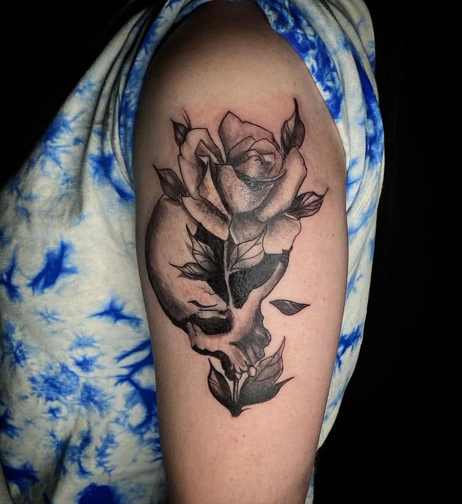 Black and grey tattoo of a skull merging into a blooming rose, symbolizing life and death, inked on the upper arm.