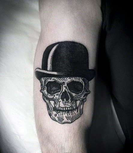 Tattoo of a skull wearing a black bowler hat on a person's upper arm