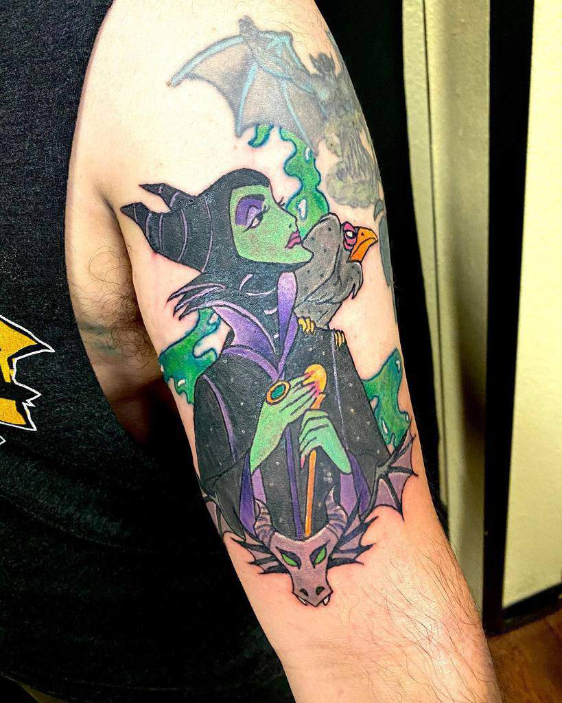 Vivid arm tattoo of Maleficent with her staff, crow companion, and dragon, surrounded by green smoke and dark magical elements