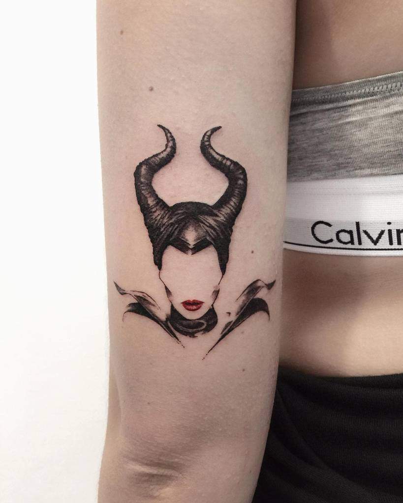 Minimalist Maleficent tattoo with bold black horns and red lips, creating a striking yet subtle design on the arm