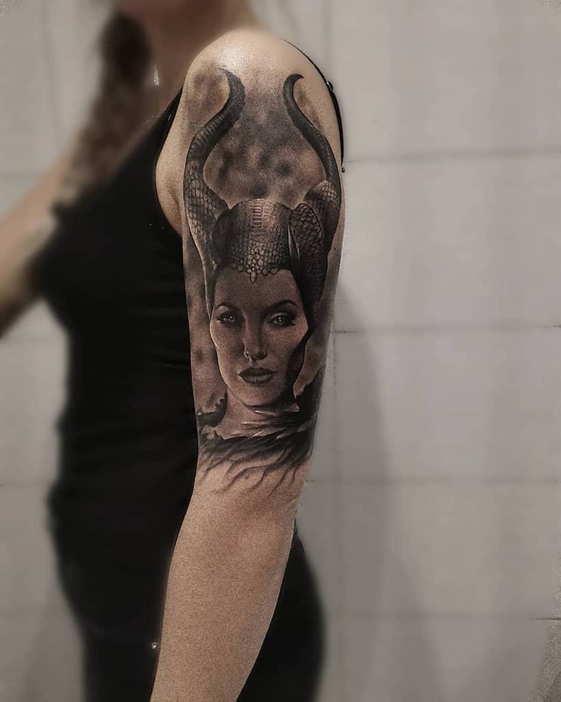 Realistic black-and-gray arm tattoo of Maleficent with detailed horns and a smoky, mysterious background, exuding dark elegance