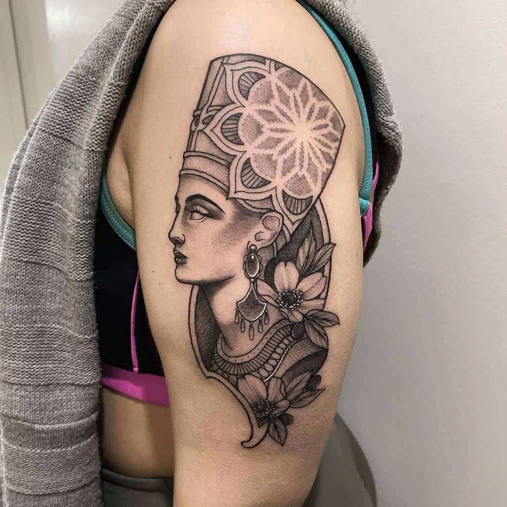 Tattoo of Queen Nefertiti with a detailed headpiece and floral design on an upper arm