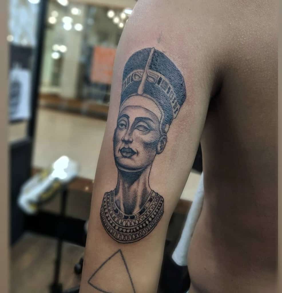 Tattoo of Nefertiti on an upper arm, featuring a detailed headdress and jewelry