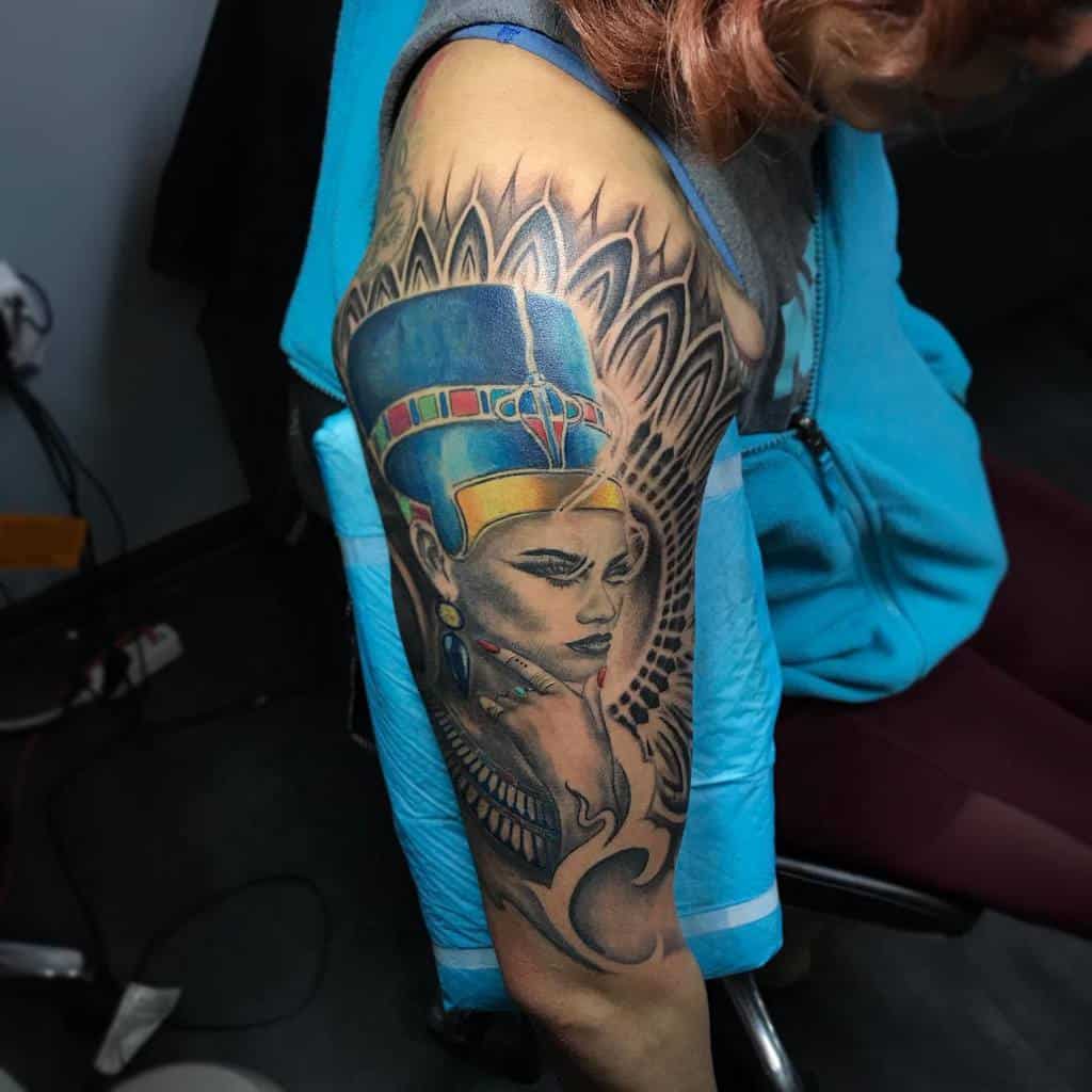 Arm tattoo showcasing Nefertiti's stylized portrait, surrounded by intricate decorative patterns
