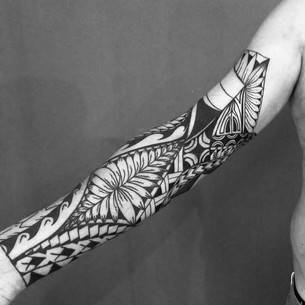 A black tribal tattoo on the arm featuring intricate patterns, including geometric shapes and stylized floral designs