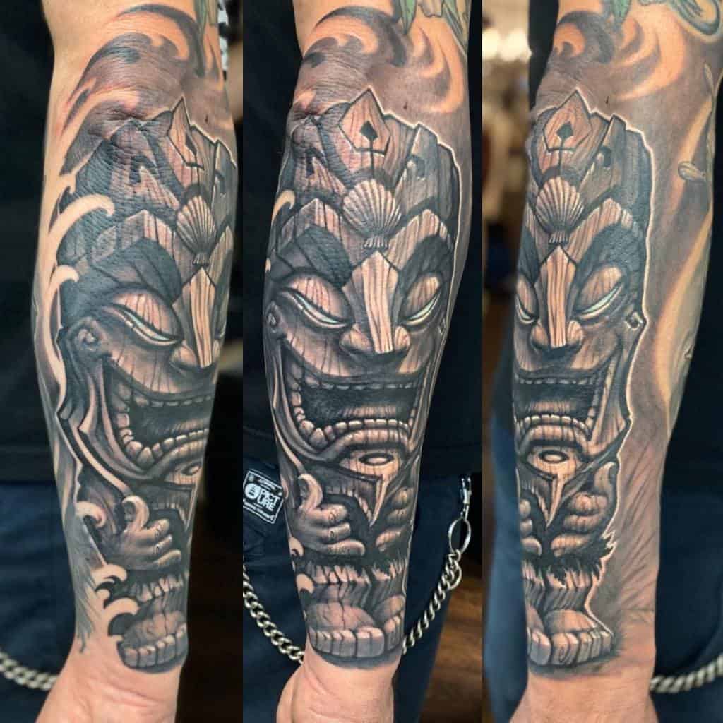 Detailed black and grey Tiki mask made of wood tattoo, showcasing intricate shading and bold lines for a dramatic effect