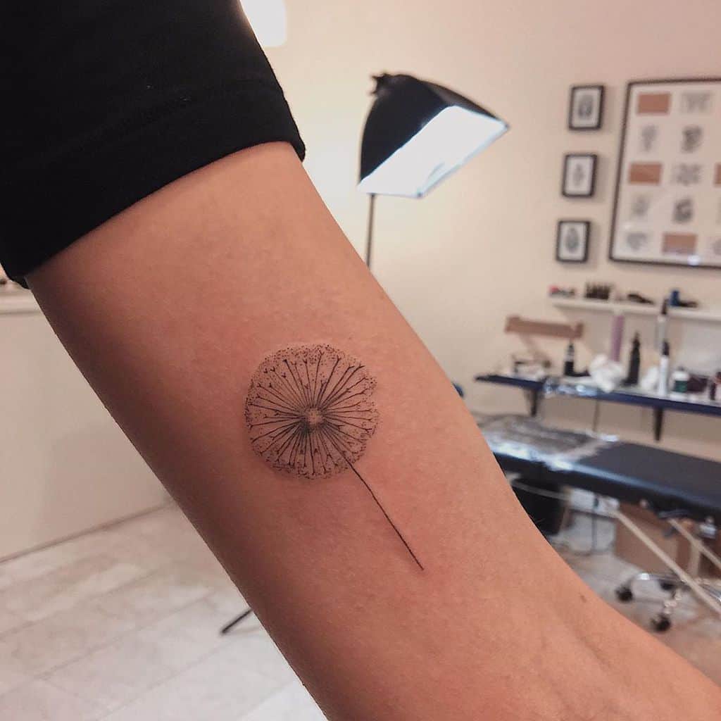 Delicate fine-line dandelion tattoo on the arm, symbolizing wishes, hope, and the fleeting nature of time.