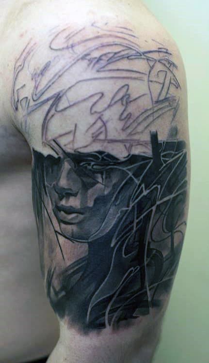 Abstract tattoo of a face with lines and shading on a person's upper arm