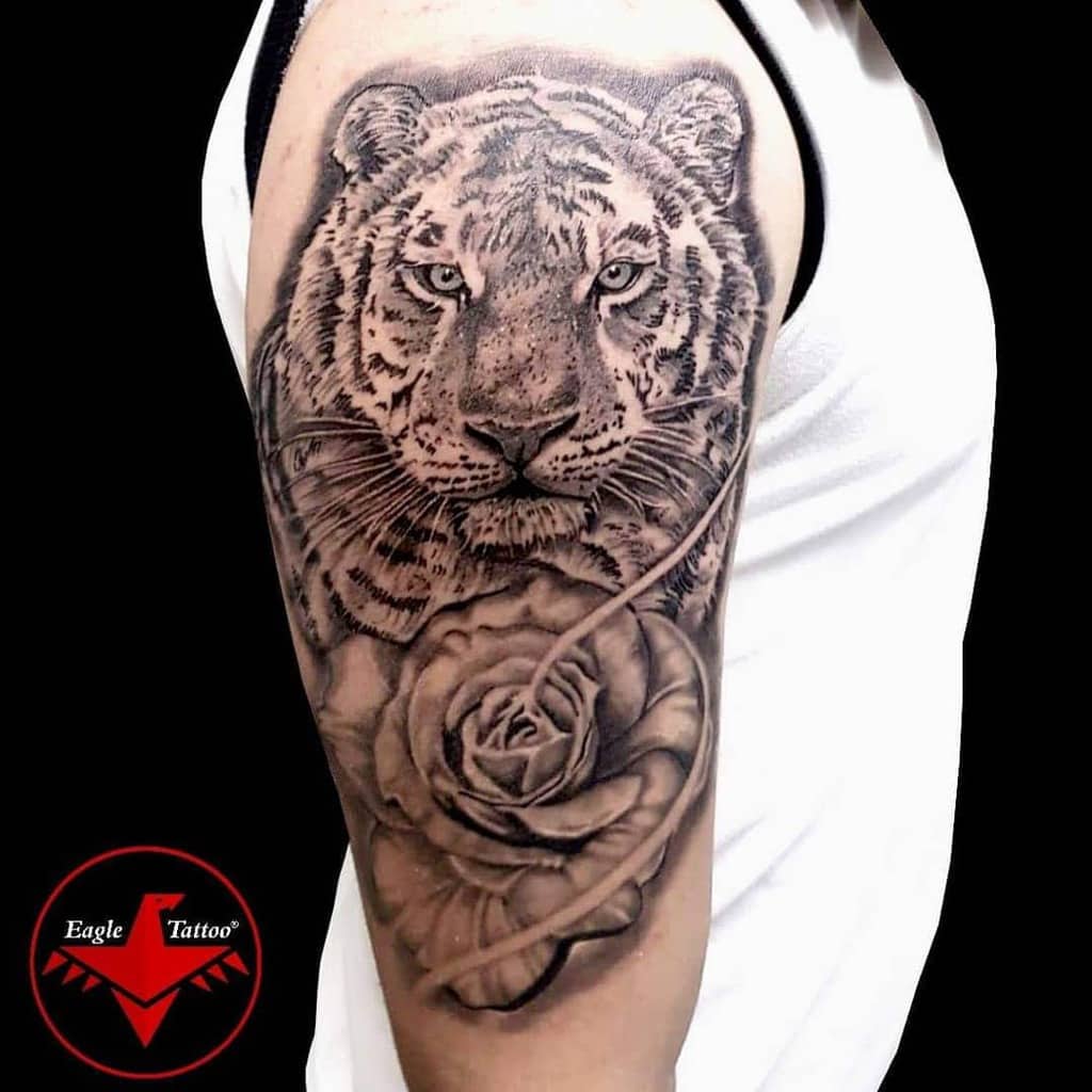 A majestic tiger poised alongside a delicate rose graces the person's upper arm, merging strength with beauty