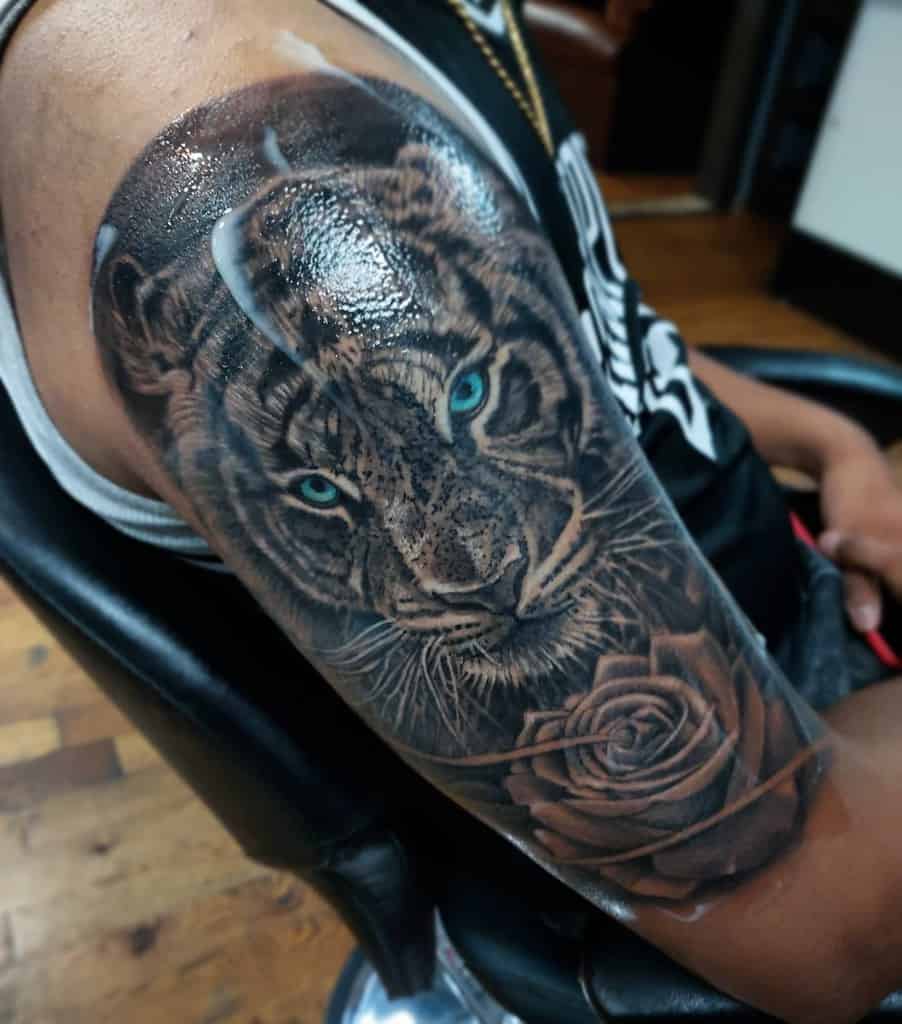 Tattoo of a tiger with blue eyes and a rose on a woman's upper arm