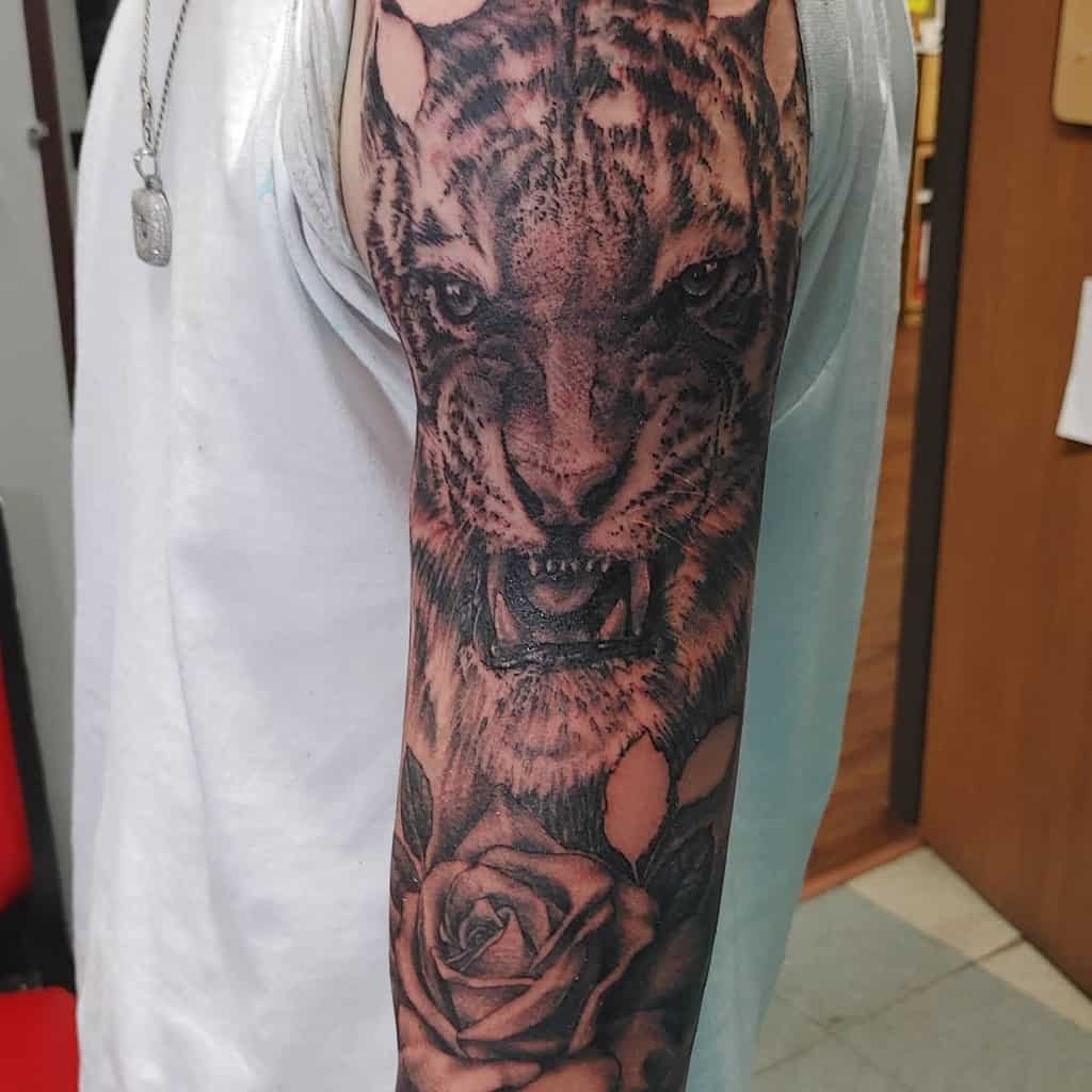 An upper arm tattoo of a fierce tiger in mid-roar, elegantly balanced with a delicate rose right below it