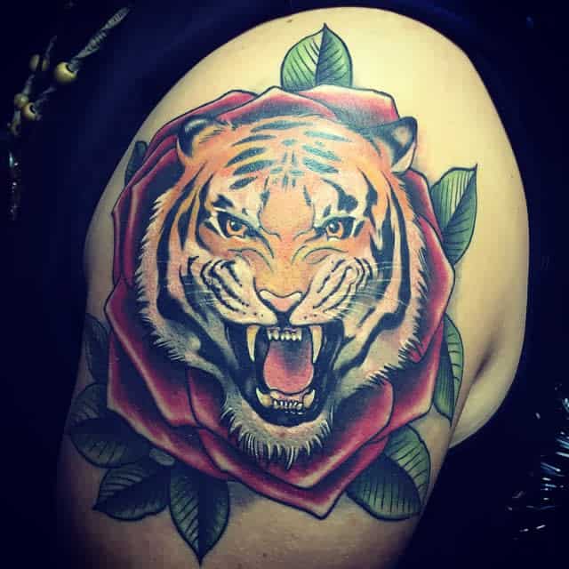 A striking tattoo of a roaring tiger's head nestled within a vibrant red rose adorns the arm