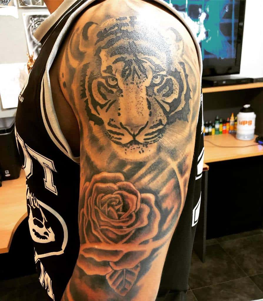 A striking tattoo of a fierce tiger intertwined with a delicate rose adorns the person's upper arm and shoulder