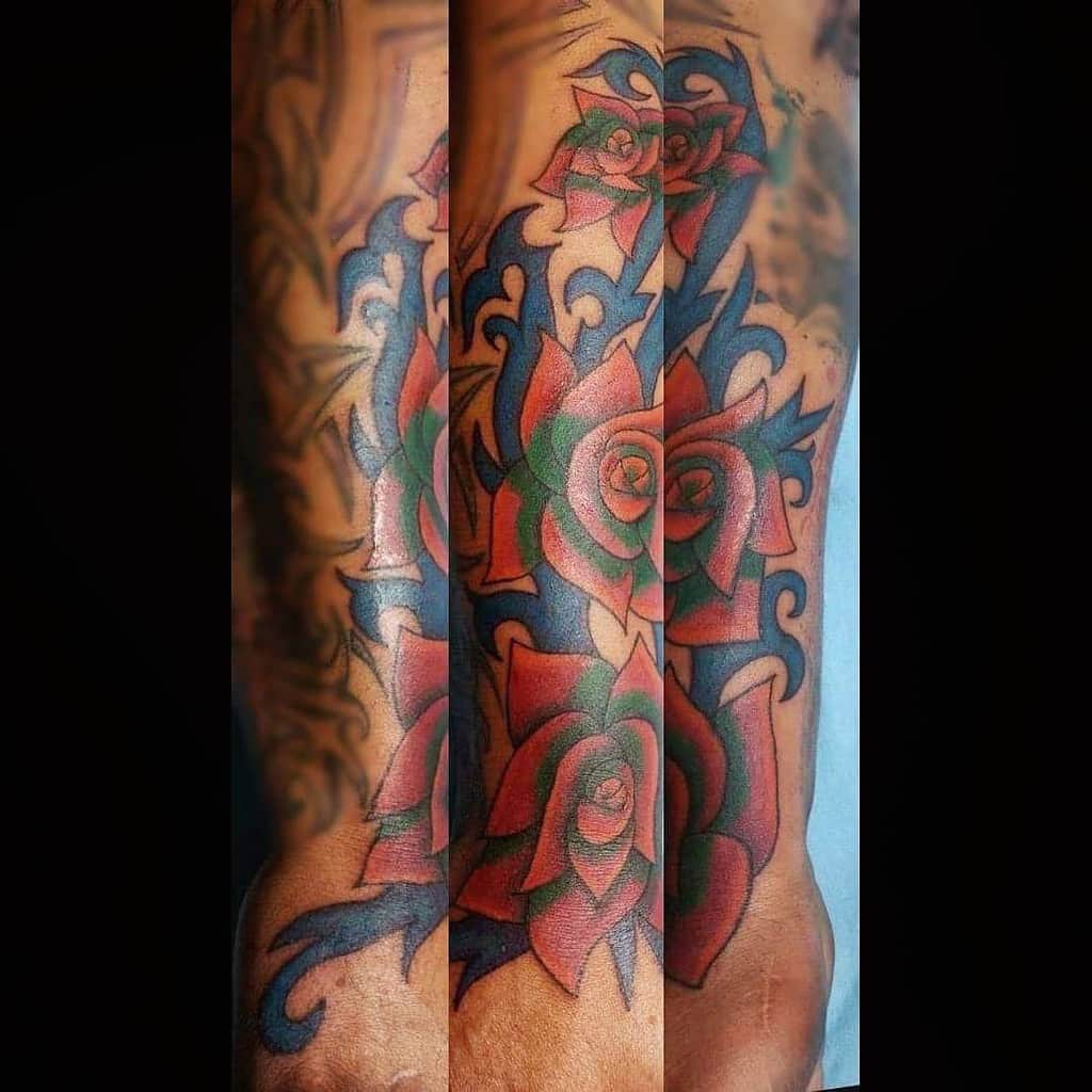 Tattoo of vibrant red roses intertwined with striking blue and black tribal designs on an arm