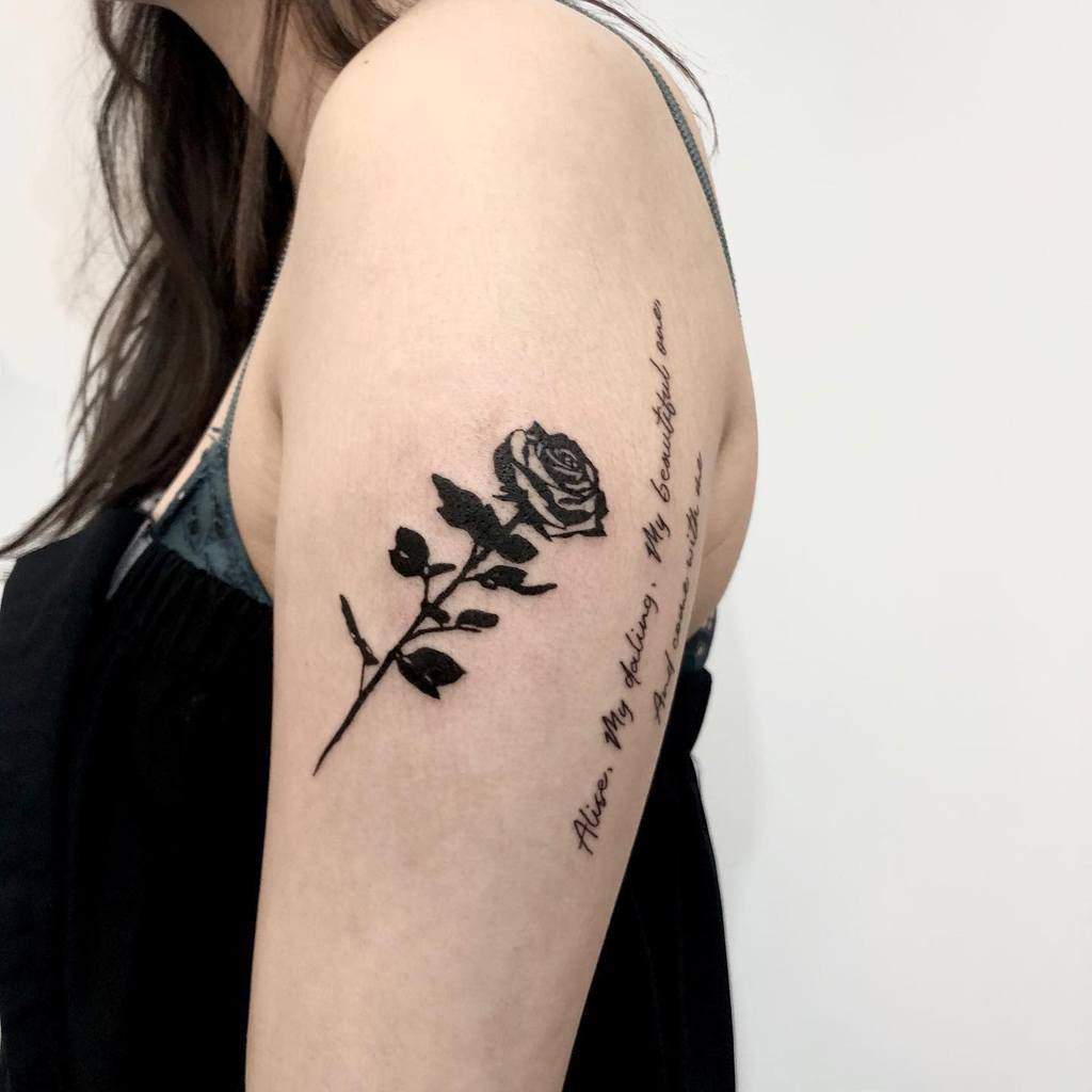 A black ink tattoo on the upper arm featuring a detailed rose stem with leaves