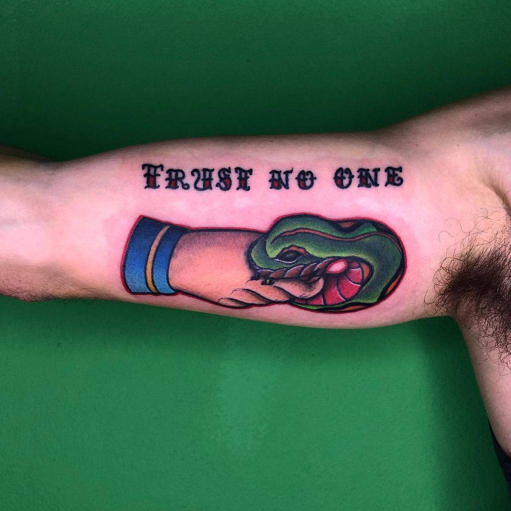 Tattoo of a hand shaking with a snake and "Trust No One" inked above on a person's arm