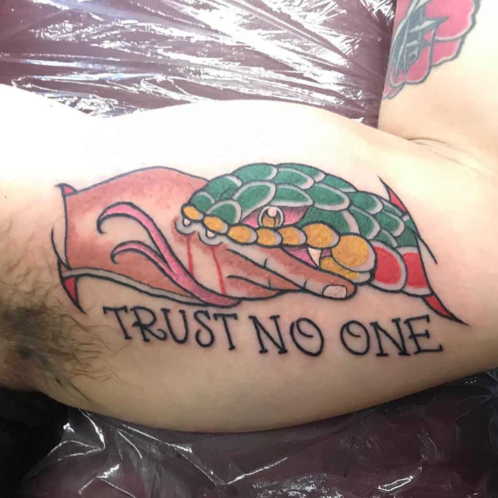 Colorful arm tattoo of a handshake where one hand is human and the other is a snake, with the phrase 'Trust No One' beneath