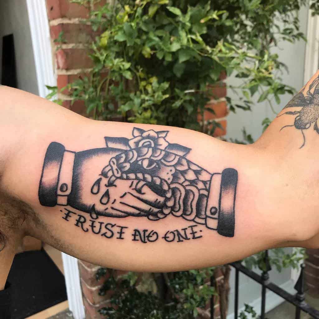 Bold blackwork tattoo featuring a handshake with a snake, 'Trust No One' text, and dripping details on the arm