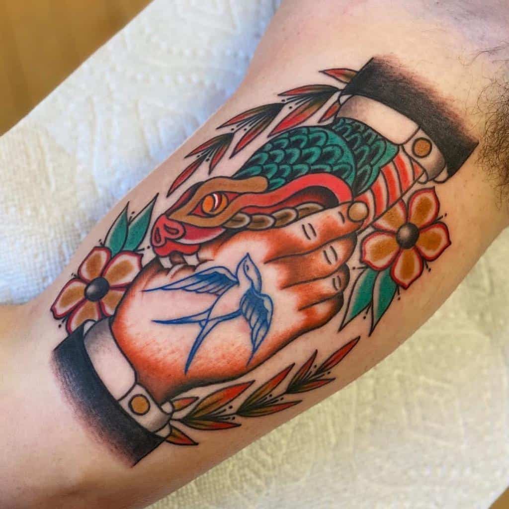 Brightly colored arm tattoo of a handshake between a human and a snake, surrounded by flowers, with a blue bird tattooed on the hand
