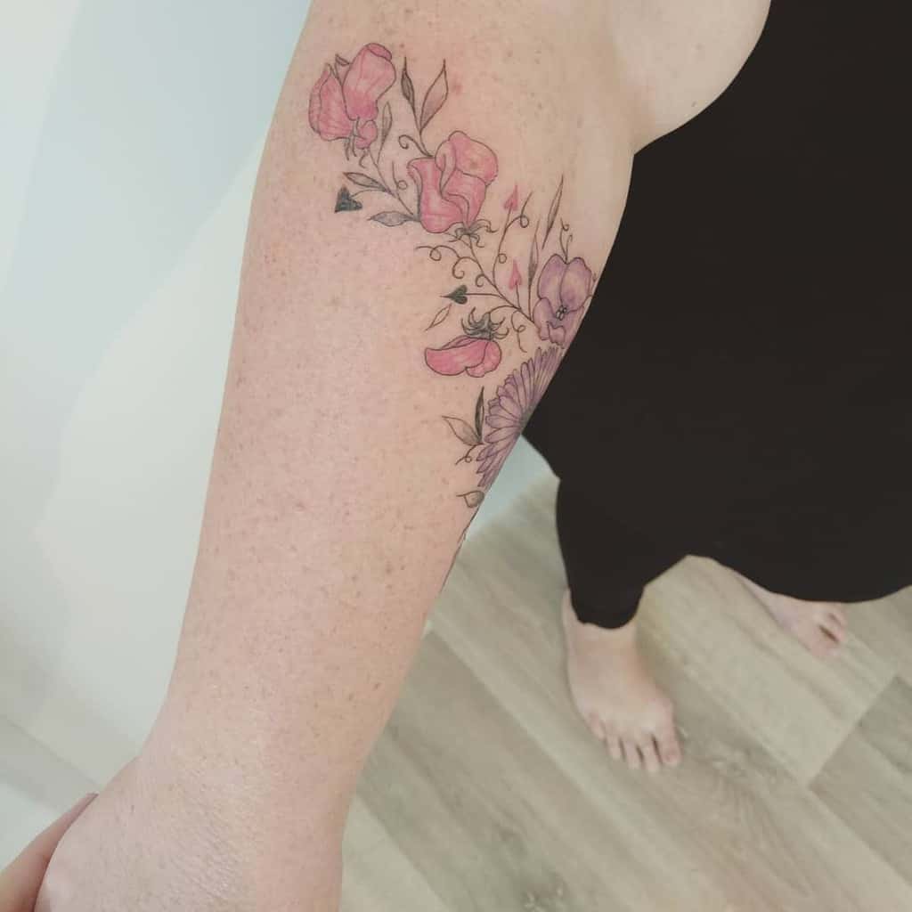 Delicate floral tattoo, featuring soft pink and violet flowers, fine-line details, and subtle shading for an elegant and feminine look