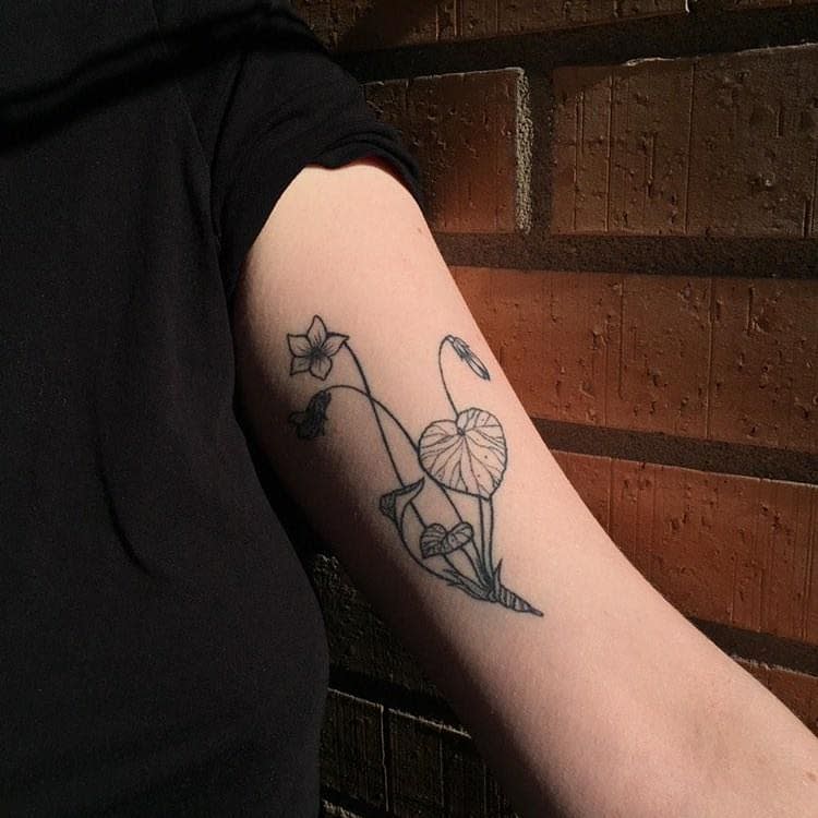 Minimalist fine-line floral tattoo, featuring delicate violet flowers and leaves, creating a natural and elegant botanical design