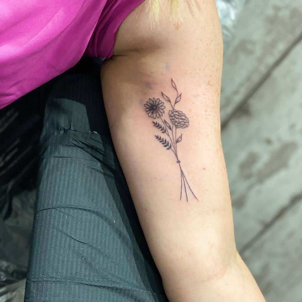 Minimalist wildflower tattoo featuring daisies and leaves in fine black ink on the inner arm, simple and elegant