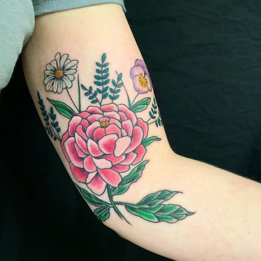 Colorful flower tattoo with leaves on a person's upper arm
