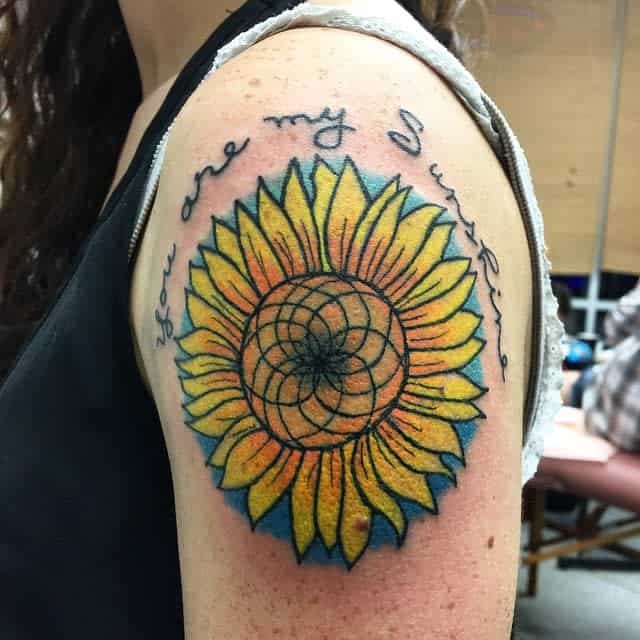 Tattoo of a sunflower with the text "You are my sunshine" on an upper arm