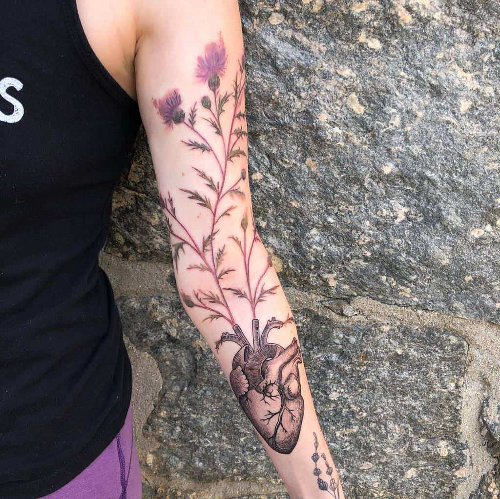 Detailed tattoo of a human heart growing into vibrant thistle flowers, covering the forearm and upper arm