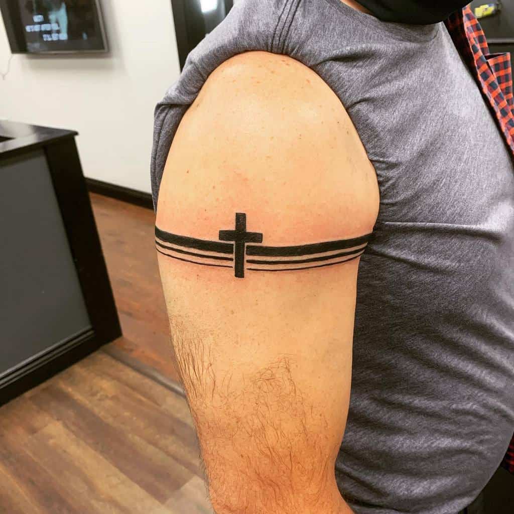 Arm tattoo with a black cross centered among three horizontal black bands on a man's upper arm