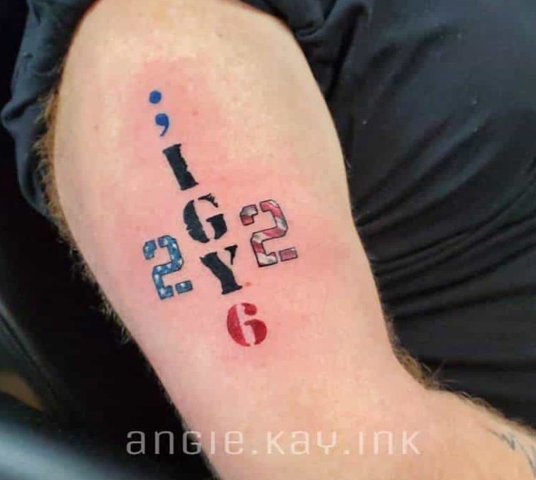 Upper arm tattoo featuring ';IGY6 22' with a blue semicolon, red 6, and numbers styled with an American flag pattern