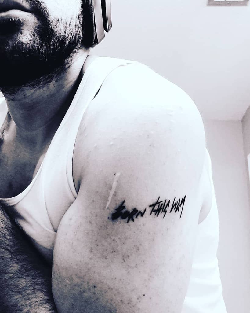 Minimalist tattoo on upper arm with 'Born This Way' text in bold, edgy lettering