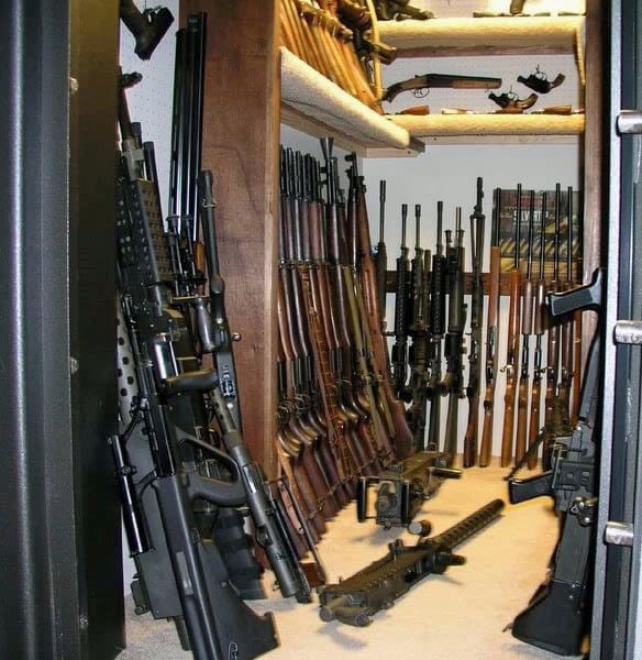 Secure armory with rifles, shotguns, and handguns displayed on wooden and pegboard racks.