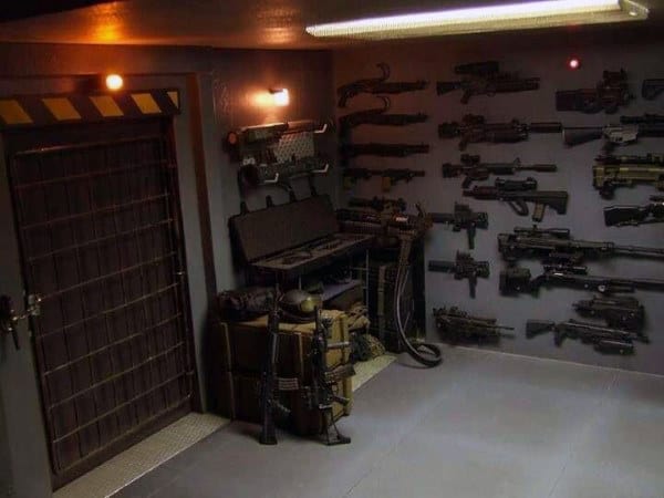 Industrial-style armory with cement floors, wall-mounted firearms, and secured metal door.