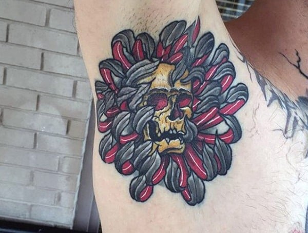 Armpit tattoo for men featuring a yellow skull surrounded by red and black twisted ribbon-like shapes in a bold traditional style.