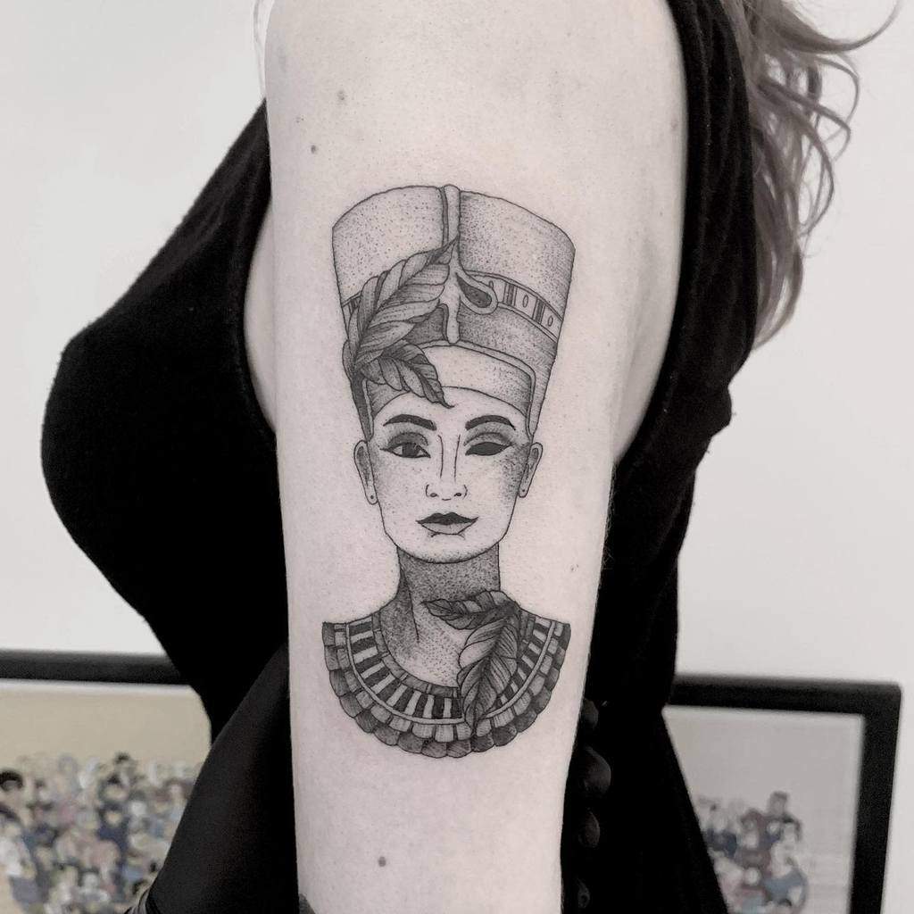 Tattoo of Queen Nefertiti's bust on a woman's upper arm in black ink