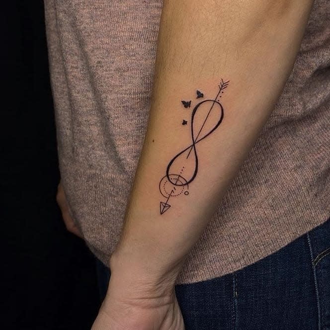 A stylish infinity tattoo featuring geometric elements, an arrow, and small birds flying within the loop, representing movement and connection.