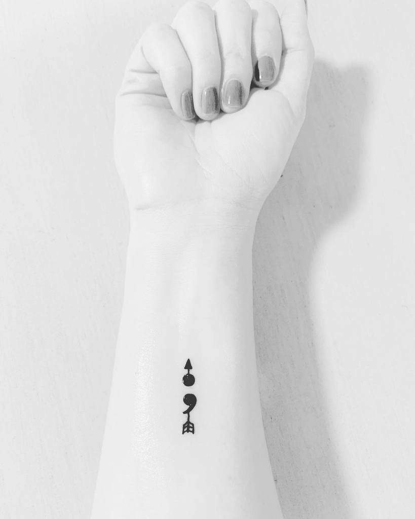 The tattoo shows a unique combination of symbols, including a semicolon and various shapes, likely representing personal meaning and resilience.