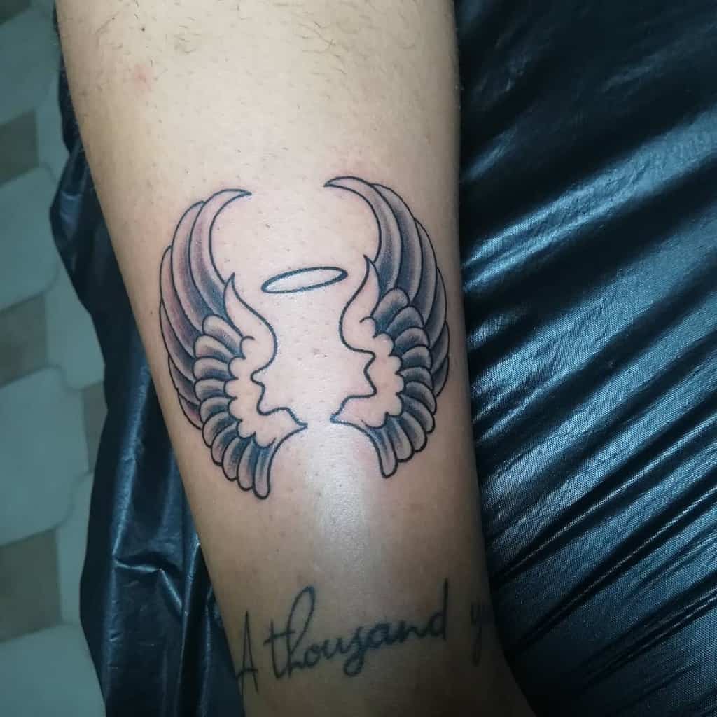 Tattoo of two wings with a halo above them accompanied by partial scripted text 'A thousand years' below