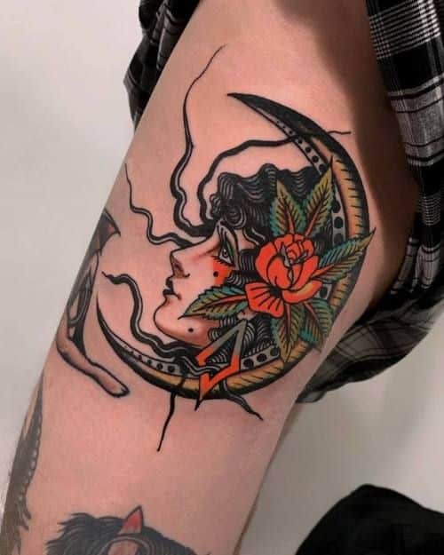 Bold tattoo of a gypsy woman framed by a crescent moon, with vibrant roses and leaves, featuring rich black shading and fine details on the arm.