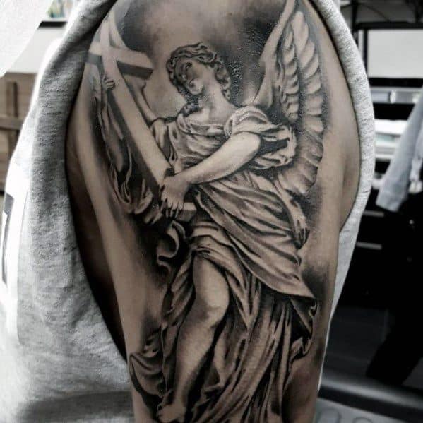 A detailed black and grey tattoo of an angel holding a sword, positioned on the upper arm of a man.