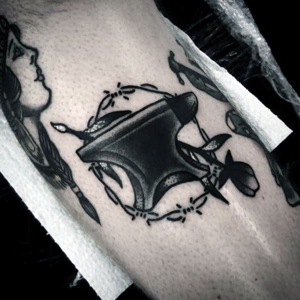 Black anvil tattoo with bold shading, wrapped in a barbed wire wreath and paired with a rose for a strong yet symbolic design.