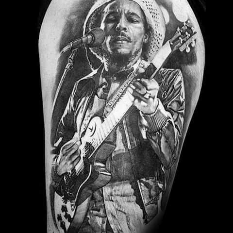 Highly detailed black and gray tattoo of Bob Marley performing with a guitar and microphone, capturing his iconic stage presence.