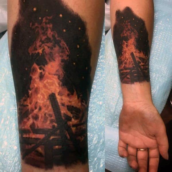 Realistic campfire tattoo with vivid flames and burning logs on the forearm, blending black and orange tones.