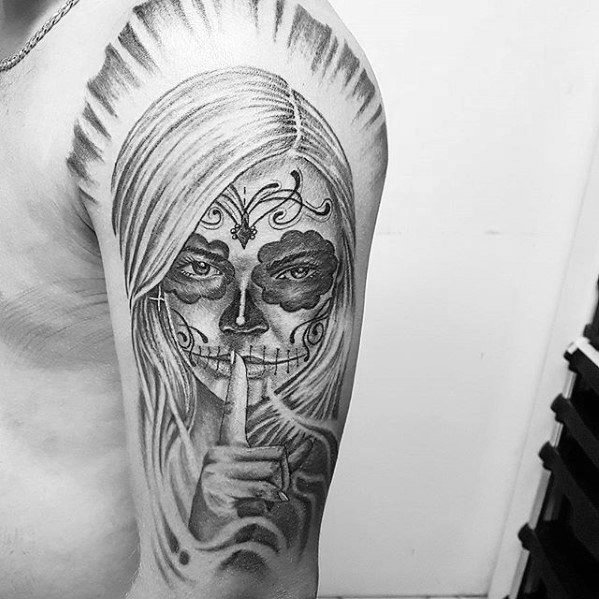 La Catrina tattoo of a woman with sugar skull makeup and flowing hair, holding a finger to her lips in a shushing gesture.