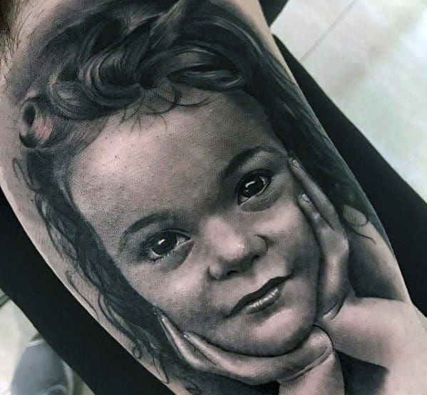 Realistic tattoo of a child resting their head on their hands, with curly hair and a serene expression
