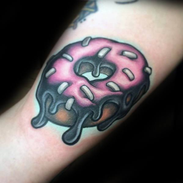 Tattoo of a pink frosted donut with white sprinkles and black melting glaze, giving it a bold and surreal look.
