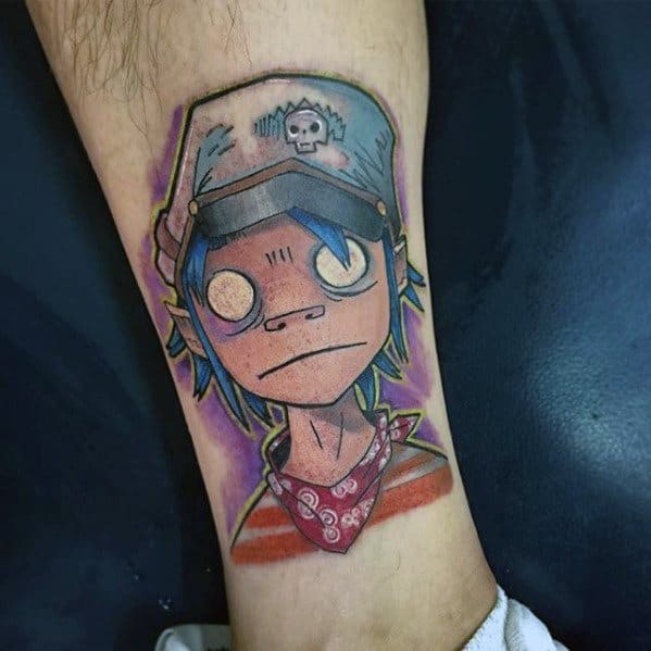 Color tattoo of 2D from Gorillaz on the lower leg, featuring wide eyes, a skull hat, red bandana, and a purple background glow.